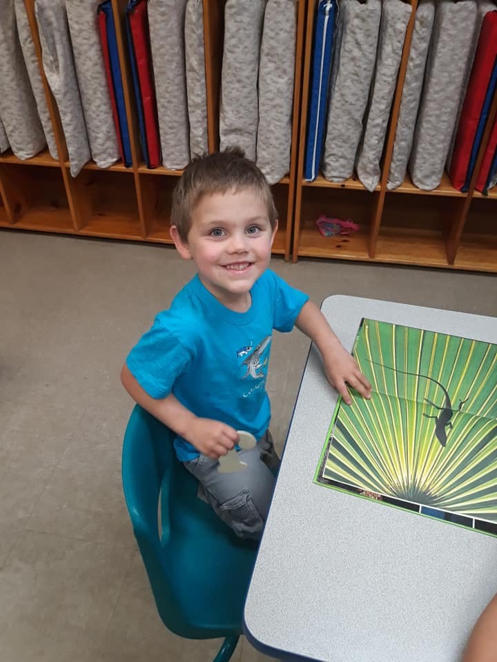 Child sitting at a table with a book, smiling