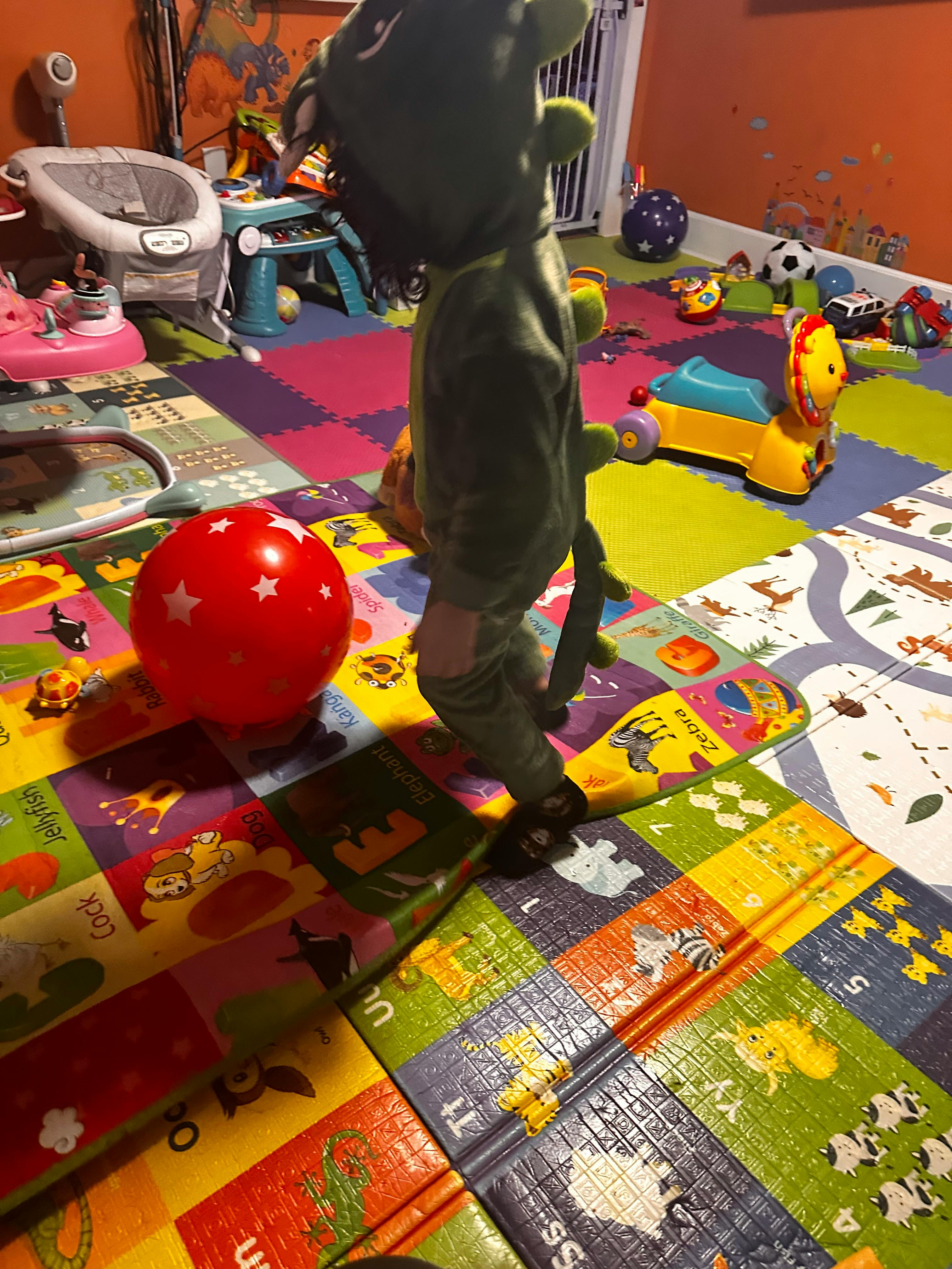 Child in green costume standing on a colorful playmat with a red ball