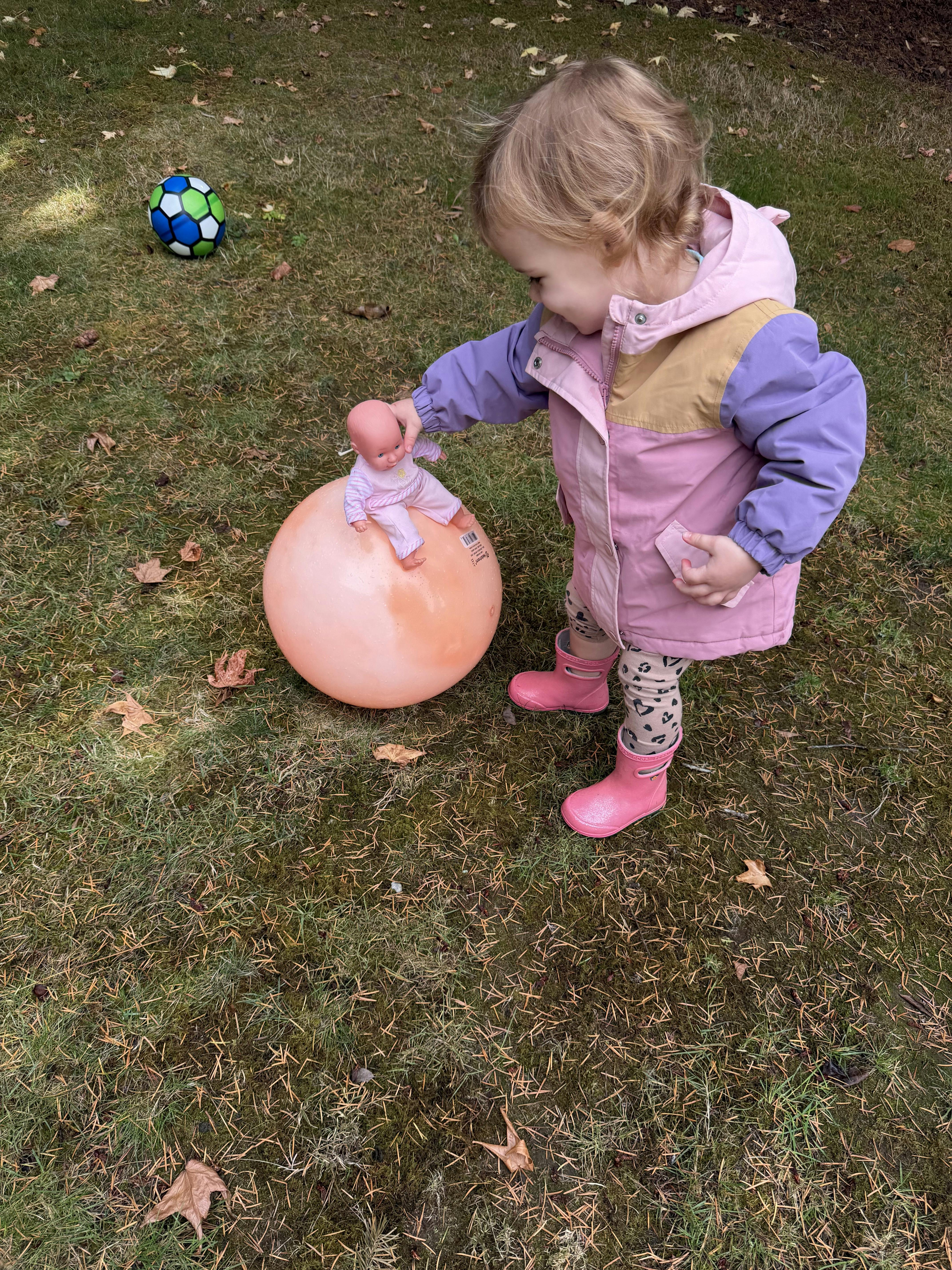 Child playing with a doll and a large ball on grass