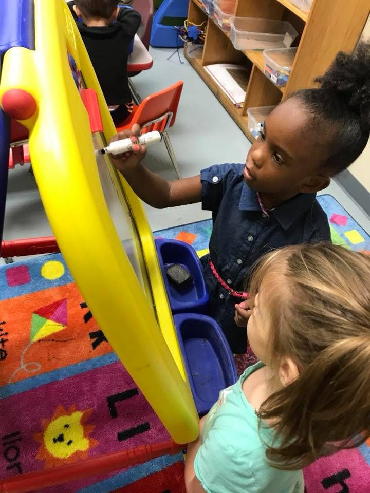 Child drawing on an easel while another child watches