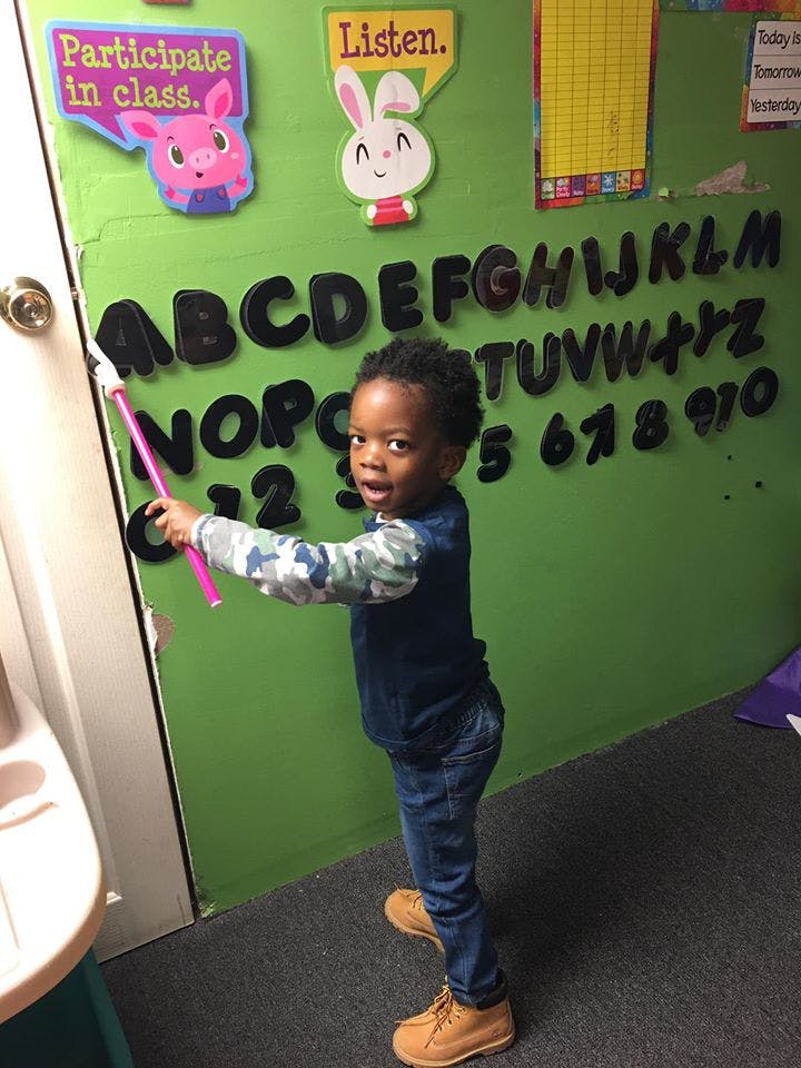 Child pointing at alphabet letters on a green wall with a pink pointer