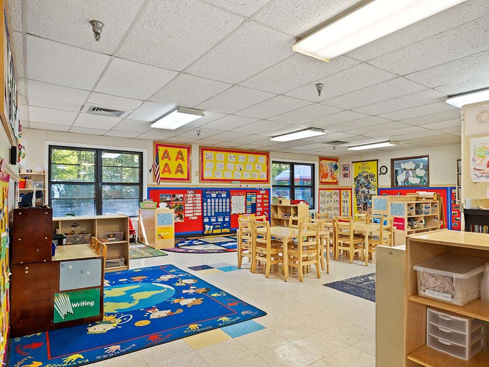 Empty classroom with small tables and chairs, colorful rugs, and learning charts