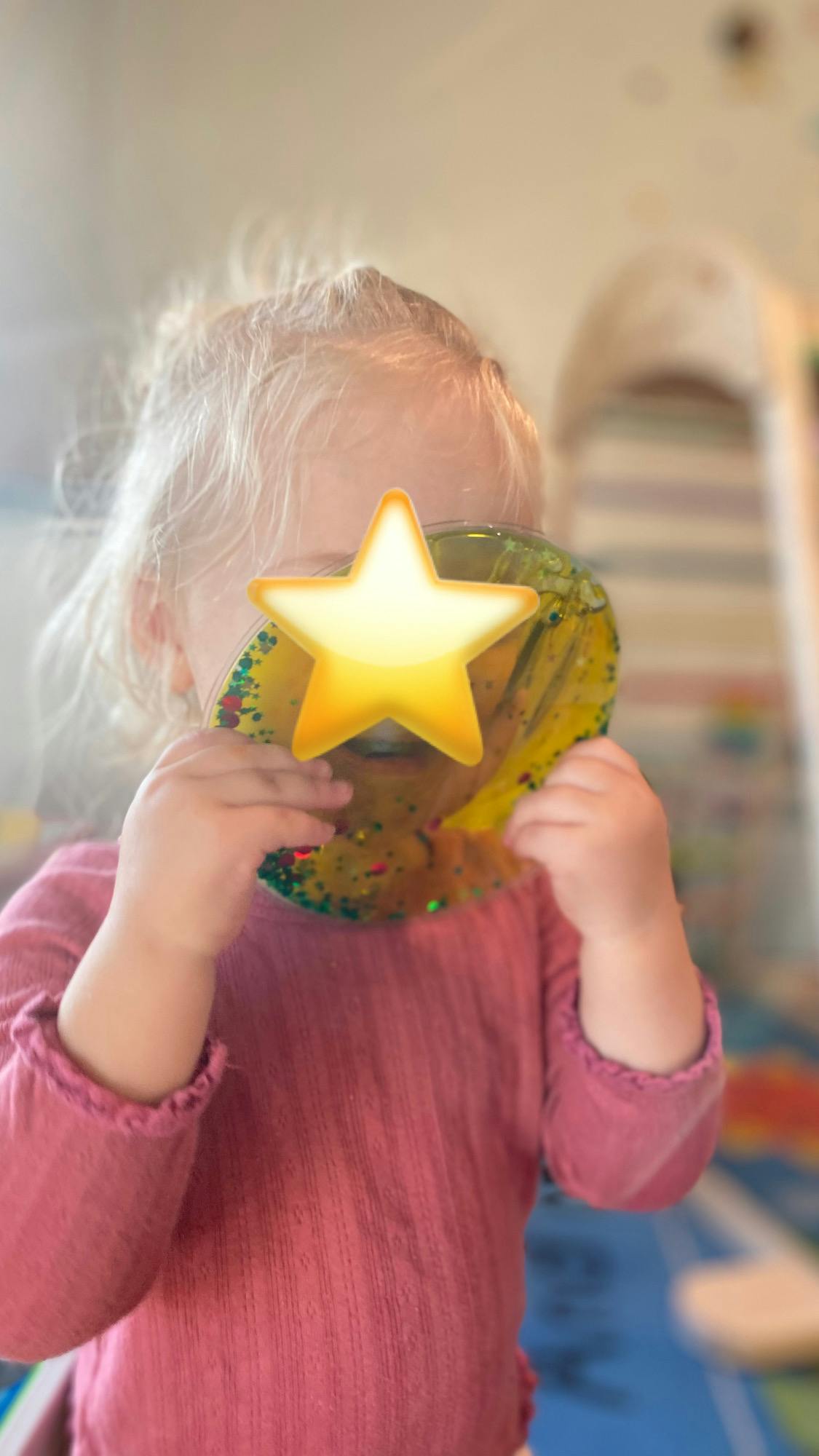 Child in a pink shirt holding a glitter sensory toy to their face