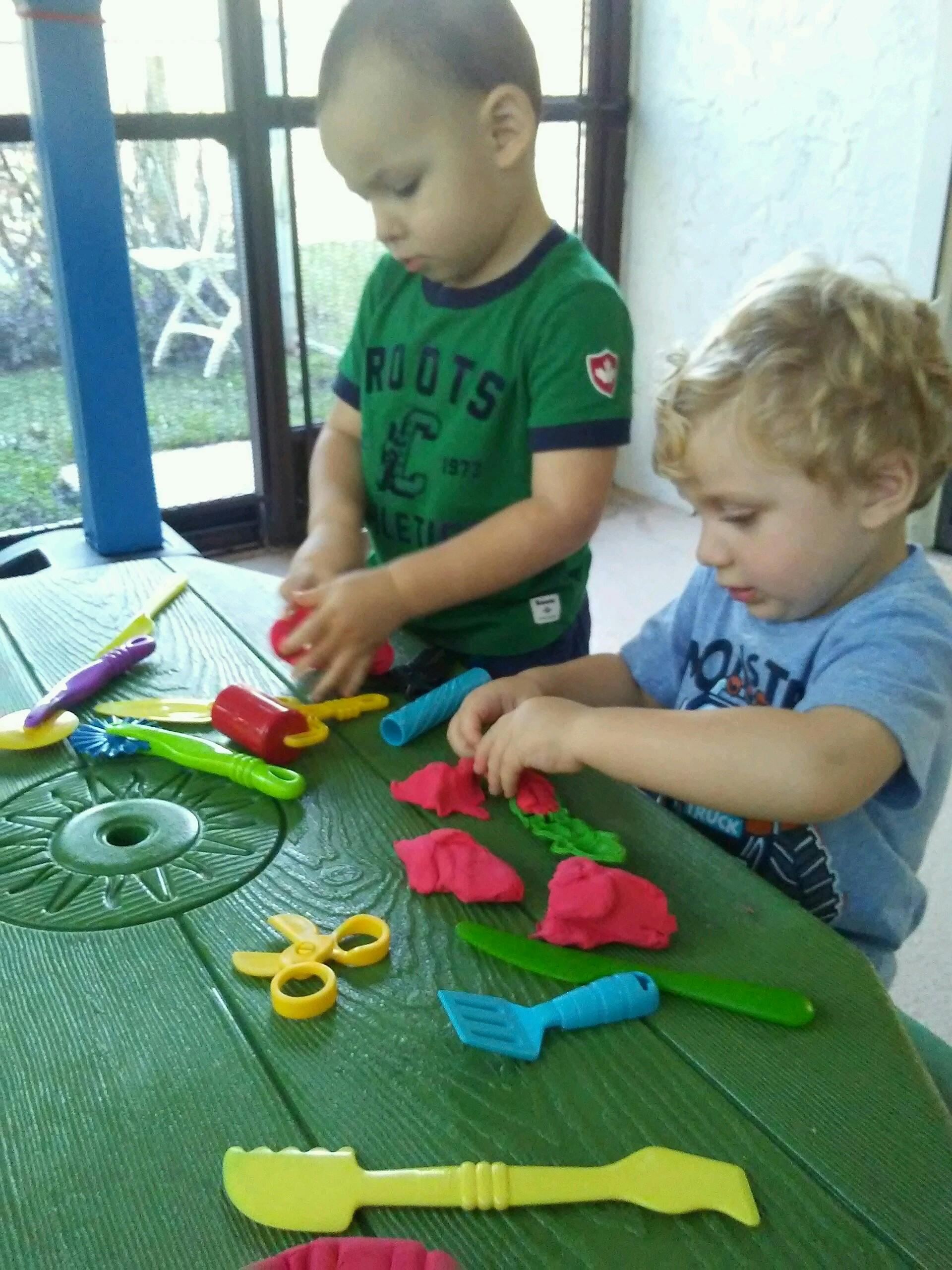 Two children playing with modeling clay and tools at a green table