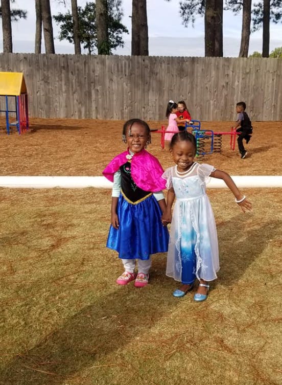 Two children in costumes holding hands on a playground
