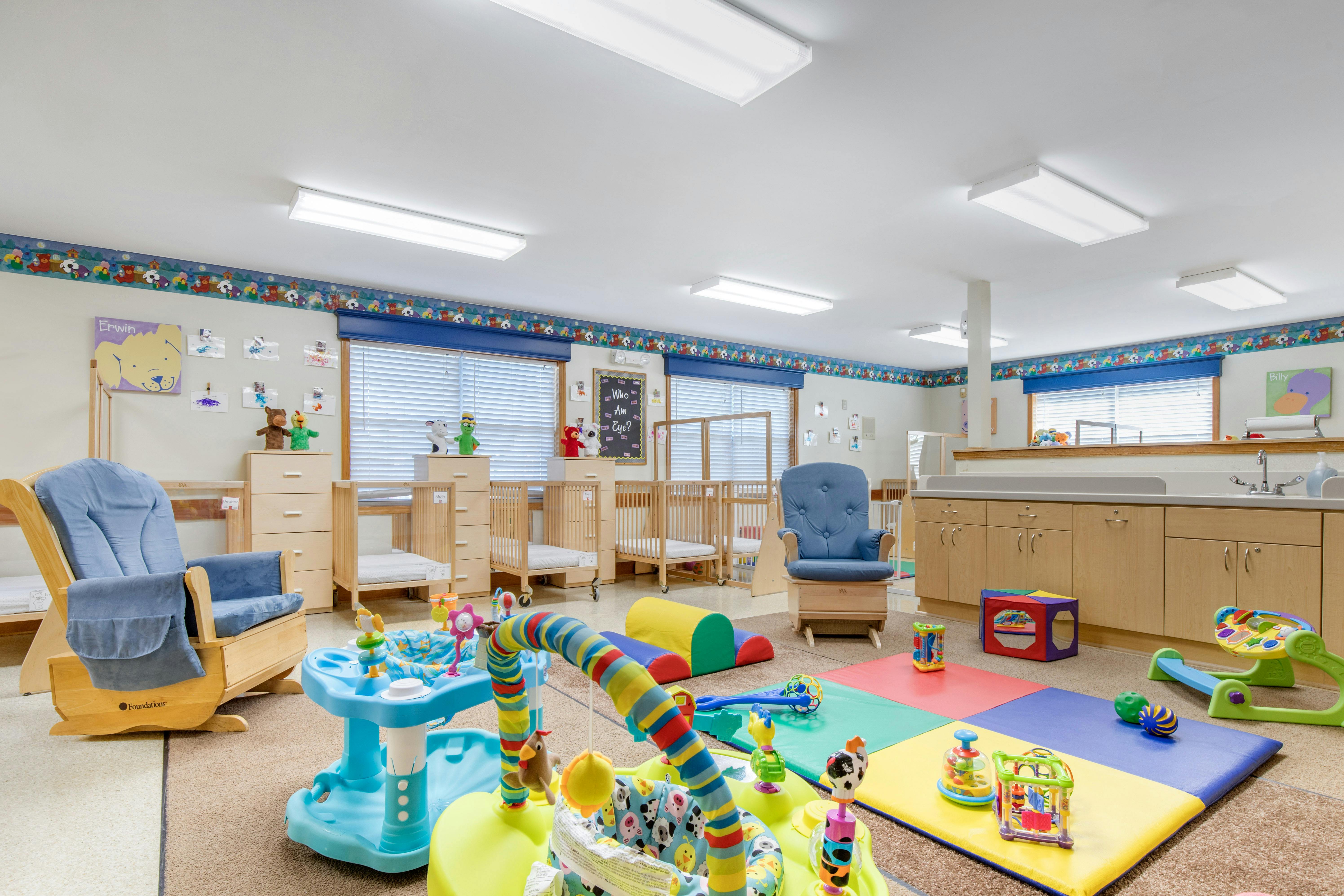 A colorful infant room with cribs, play mats, and toys