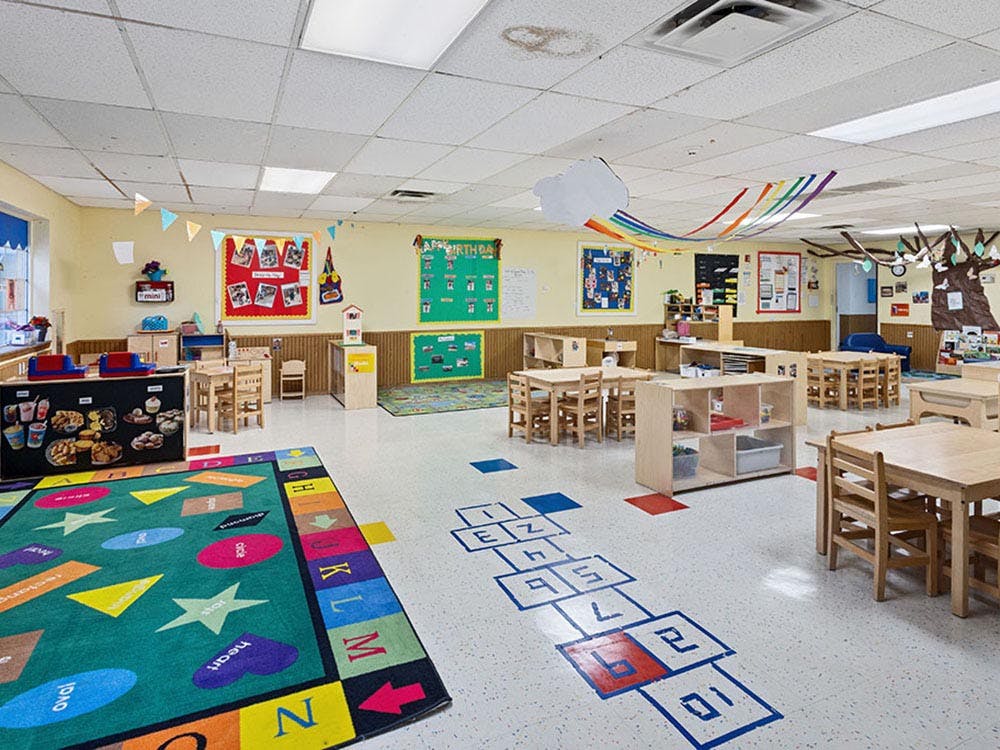 Empty colorful preschool classroom with small tables, chairs, and rugs