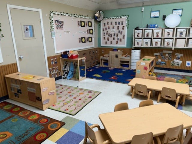 Empty classroom with small tables and chairs, play kitchen, and rugs