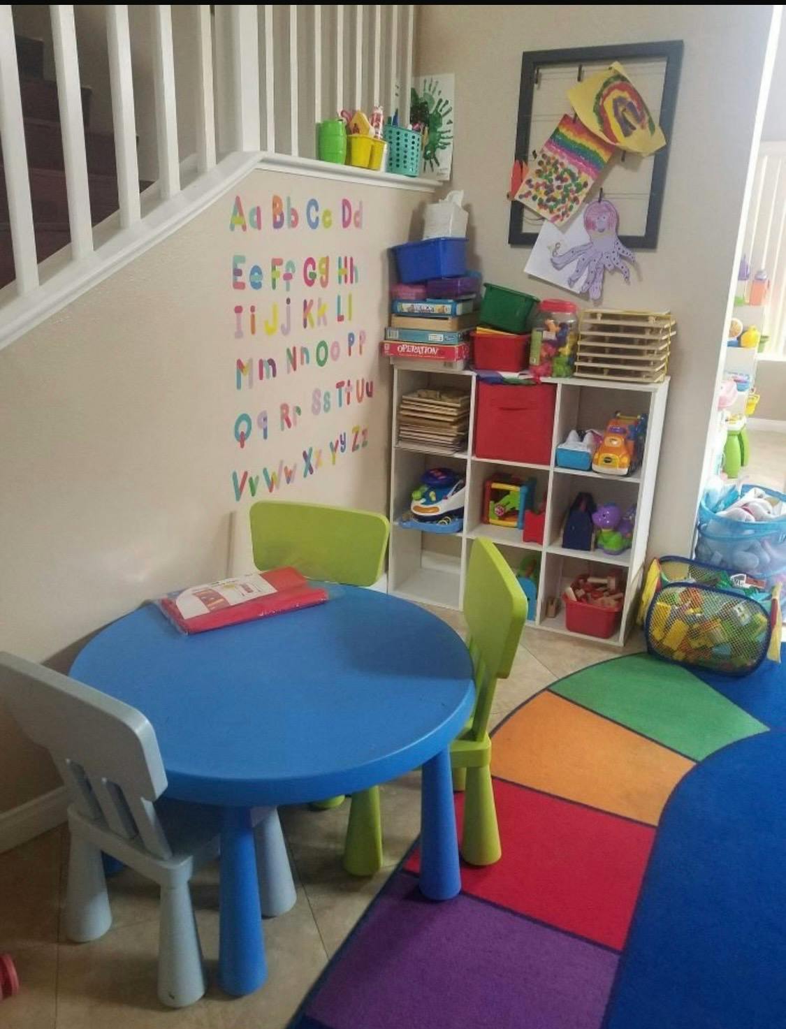 Play area with a blue table, chairs, toy shelf, and alphabet wall decal