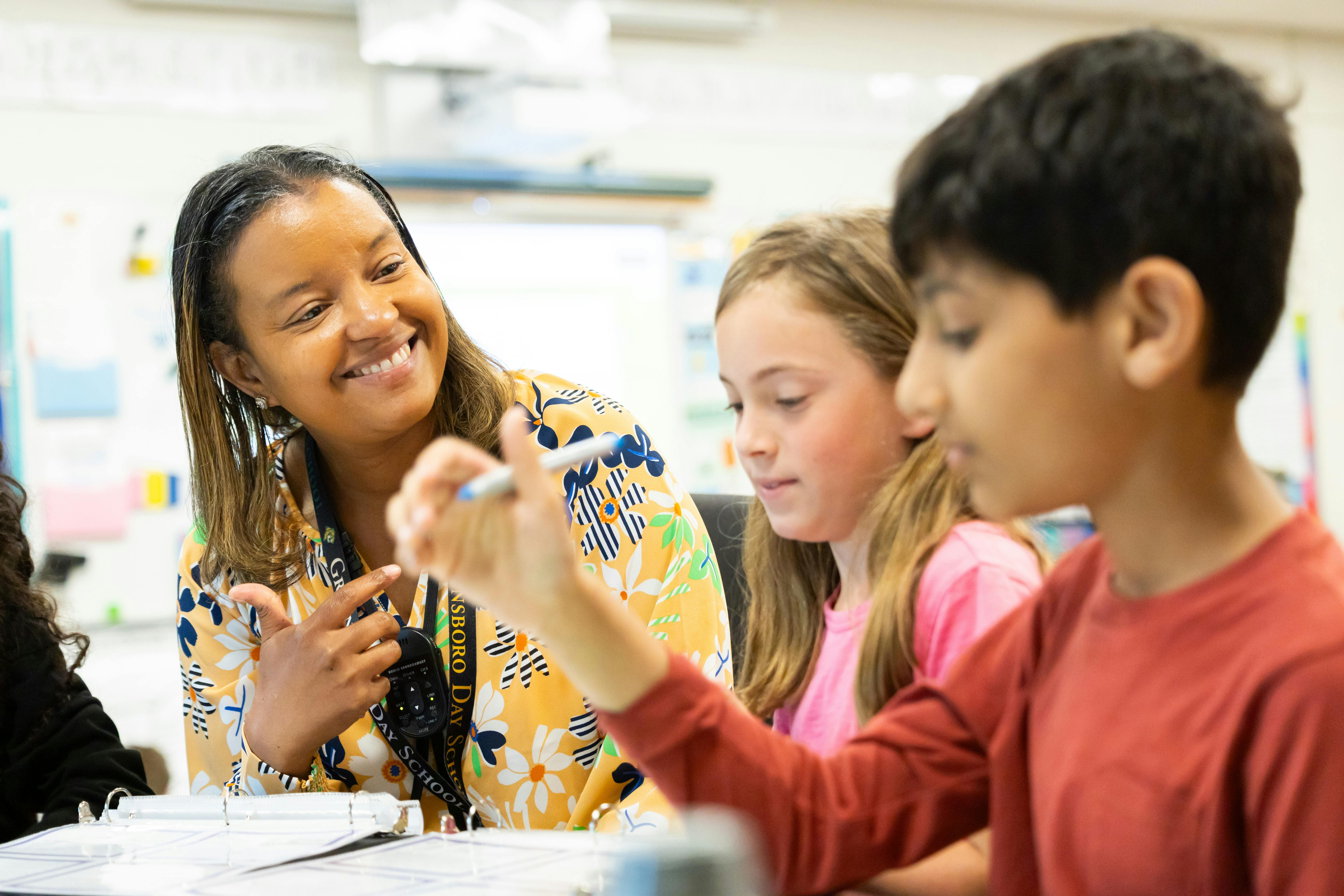 Adult assisting two children with schoolwork in a classroom