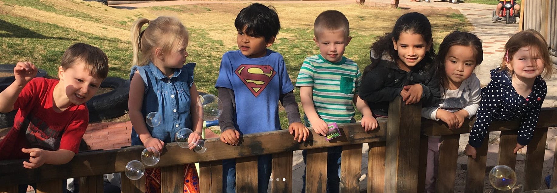 Group of children looking over a wooden fence
