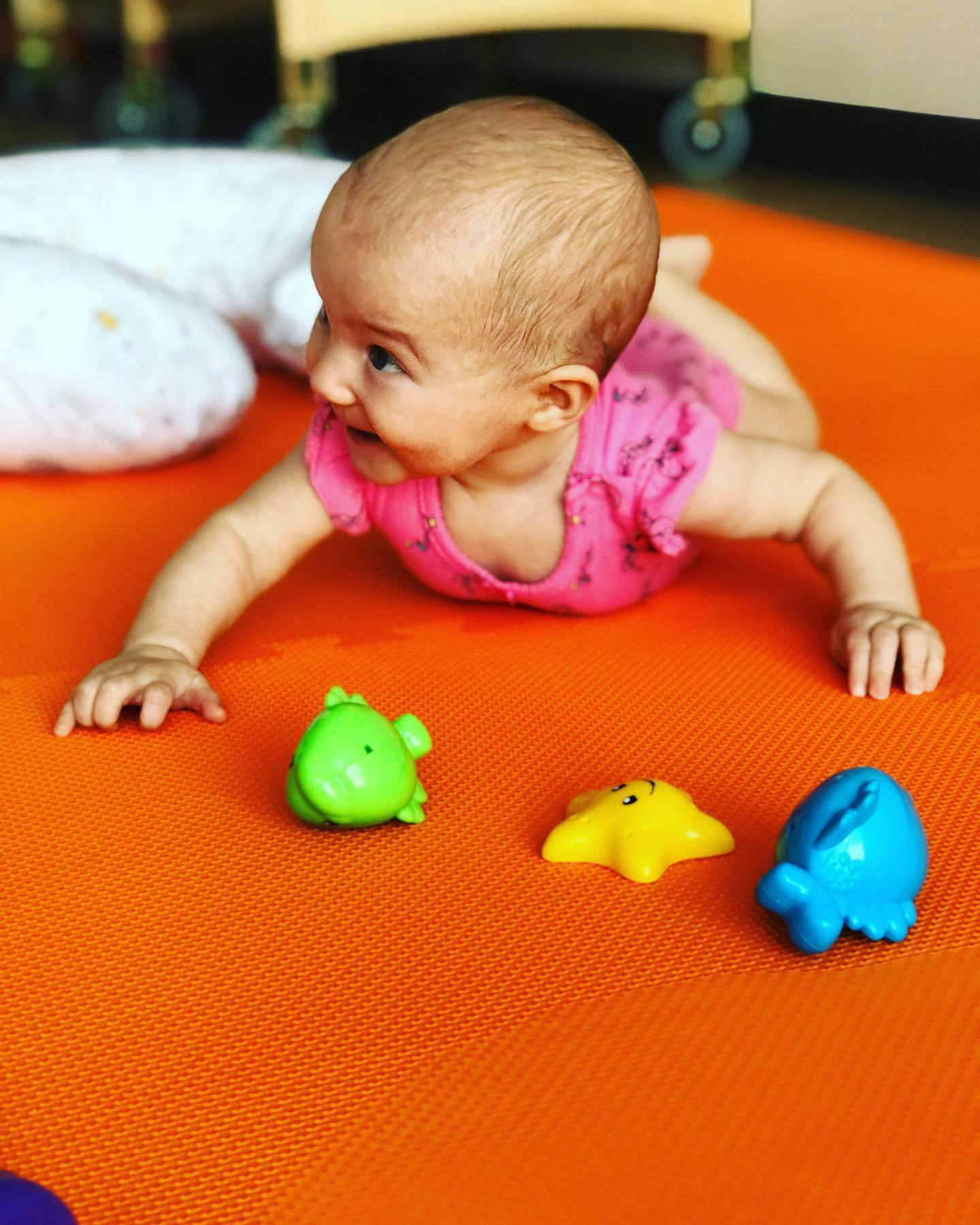 Child on stomach on orange mat with three toys