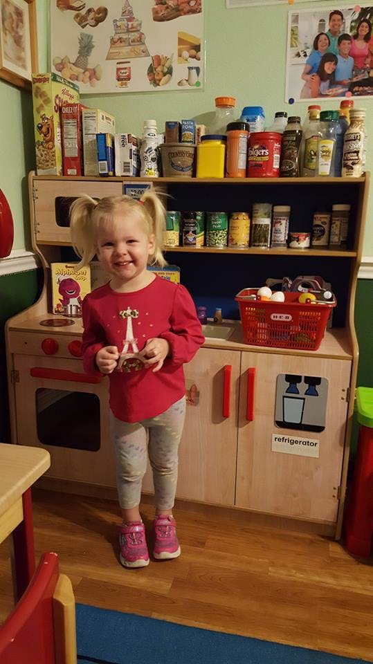 Child smiling in front of a toy kitchen