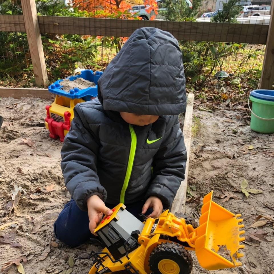Child playing with a toy construction vehicle in a sandbox