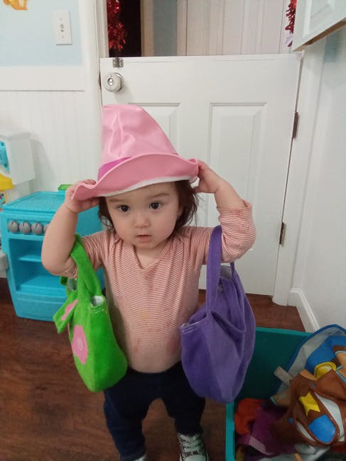 Child wearing a pink hat and holding two bags