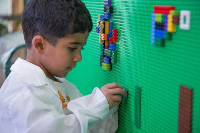 Child in a white shirt building with colorful blocks on a green wall