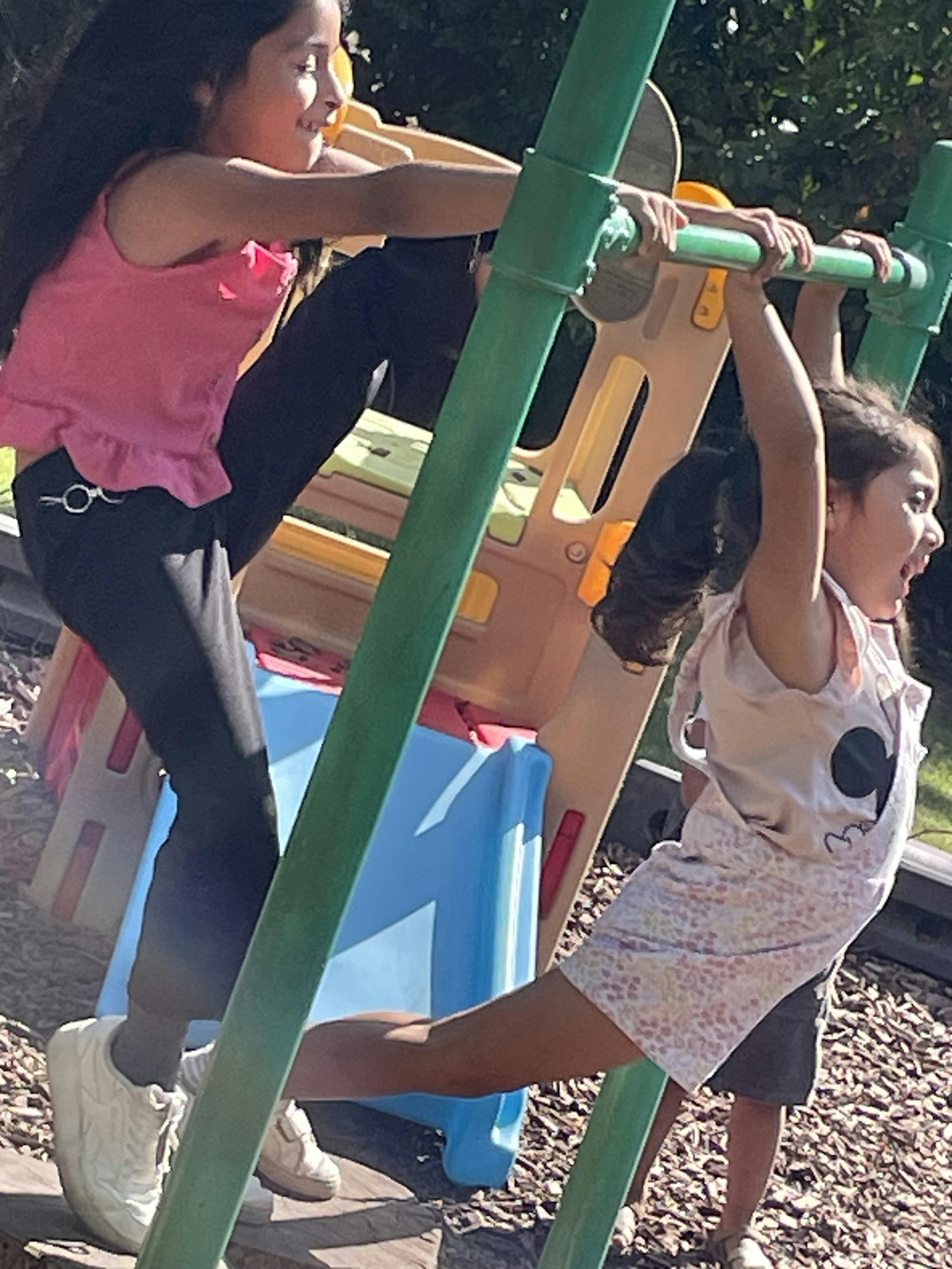 Two children playing on a jungle gym in a playground