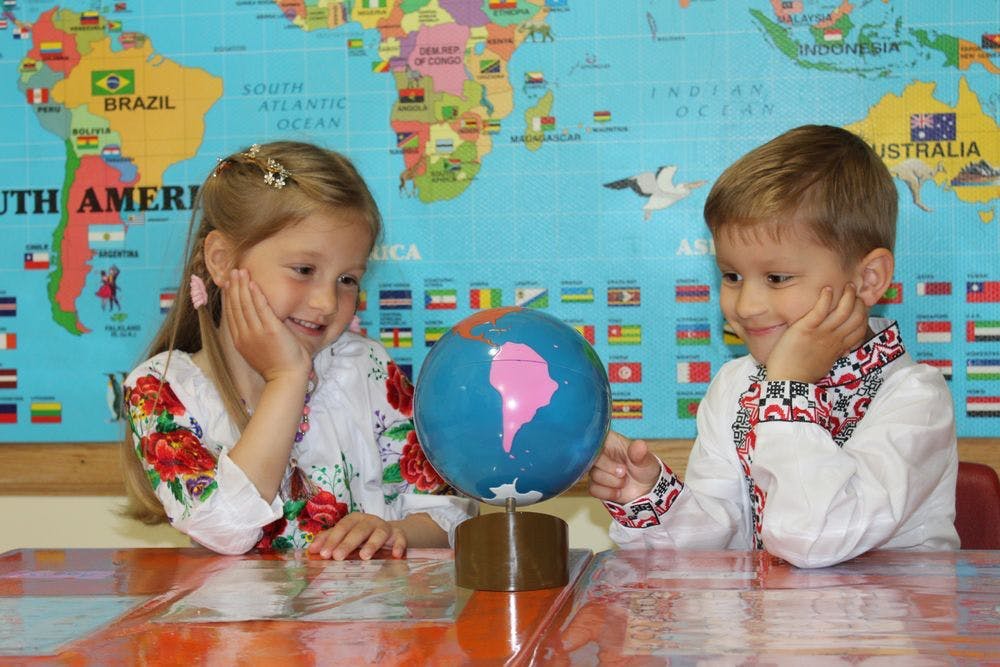 Two children looking at a globe in front of a world map