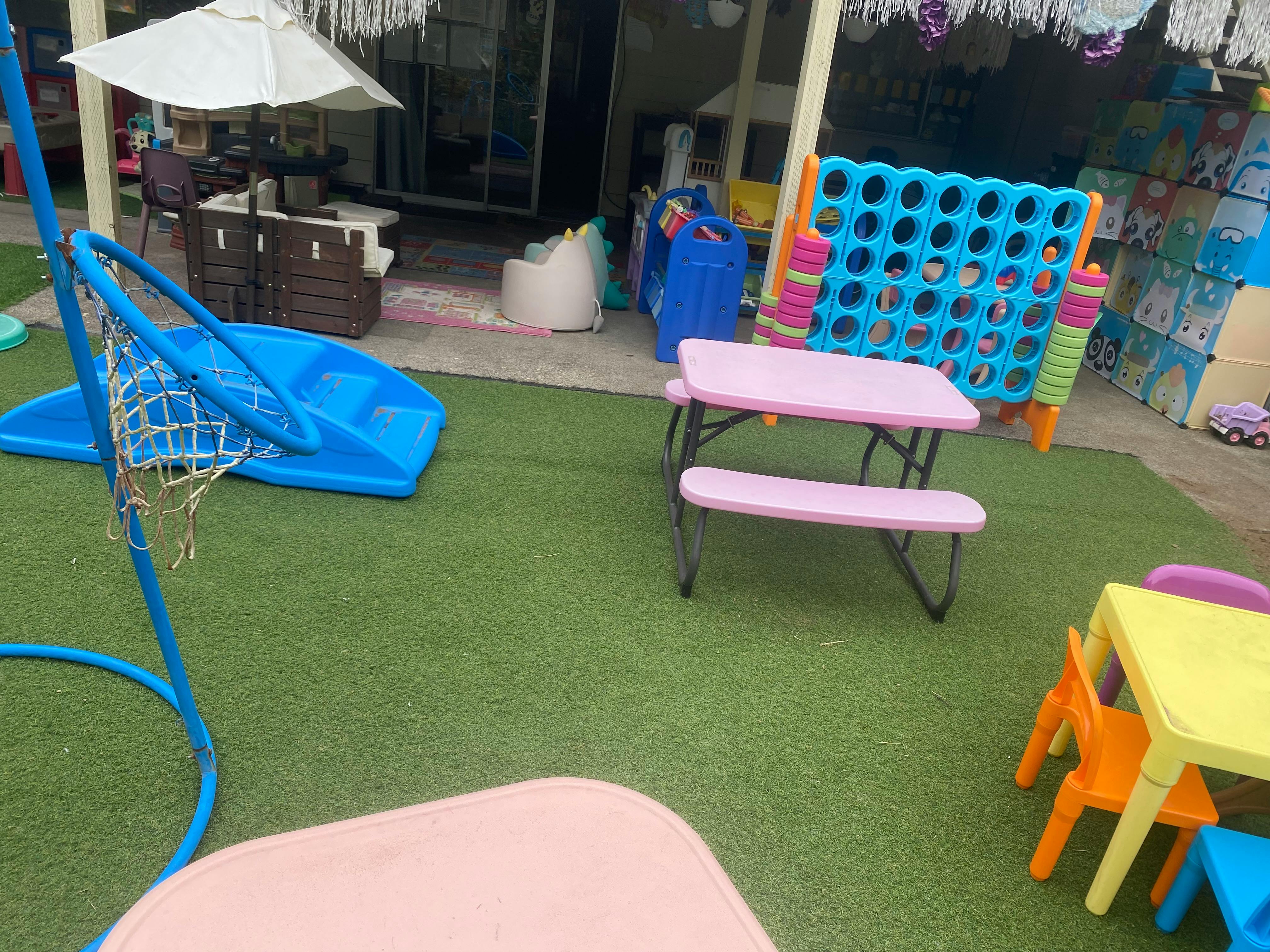 Outdoor play area with a blue basketball hoop, slide, and children's tables