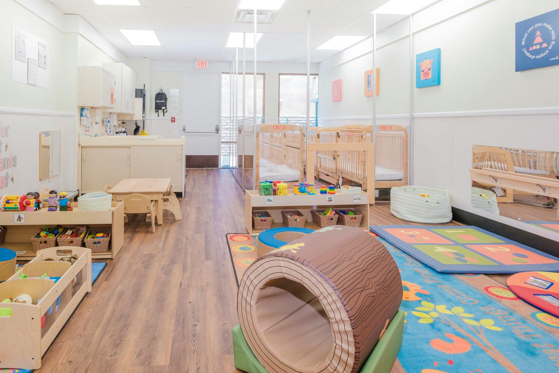 A brightly lit nursery with several cribs, a play area, and small furniture