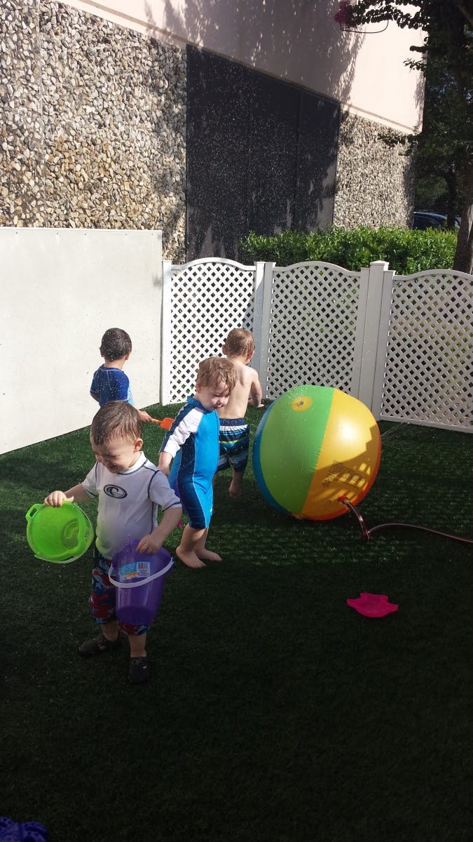 Children playing with a large beach ball and buckets on artificial grass