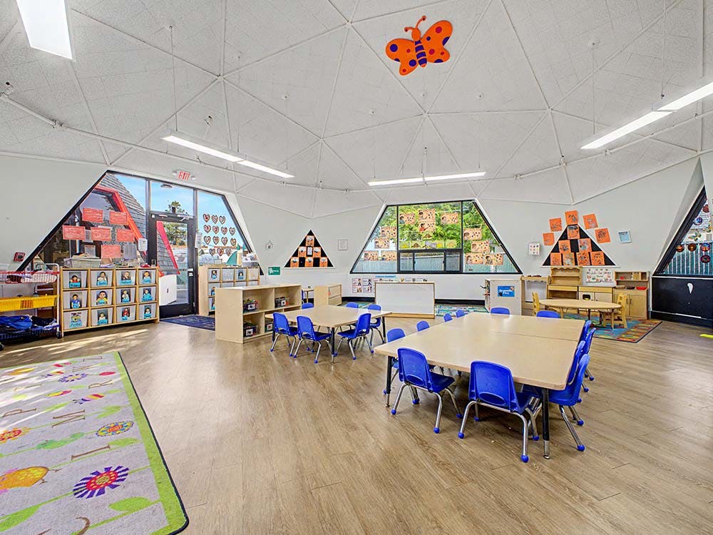 Empty classroom with small tables and chairs, and large triangular windows