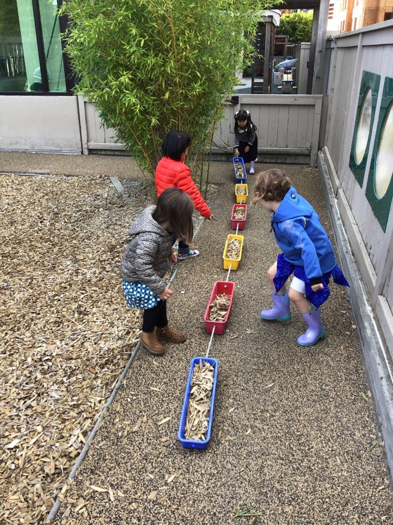 Children playing with a line of colorful containers filled with wood chips