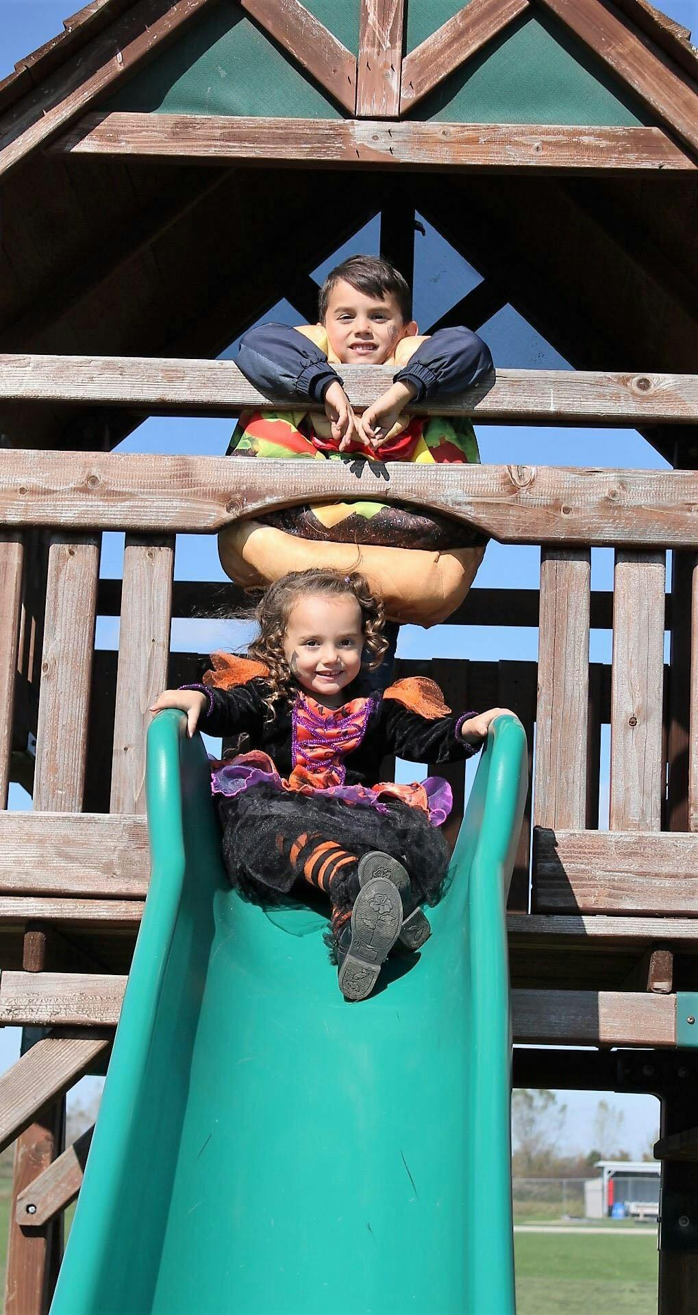Child on a slide below a teen on a playground structure