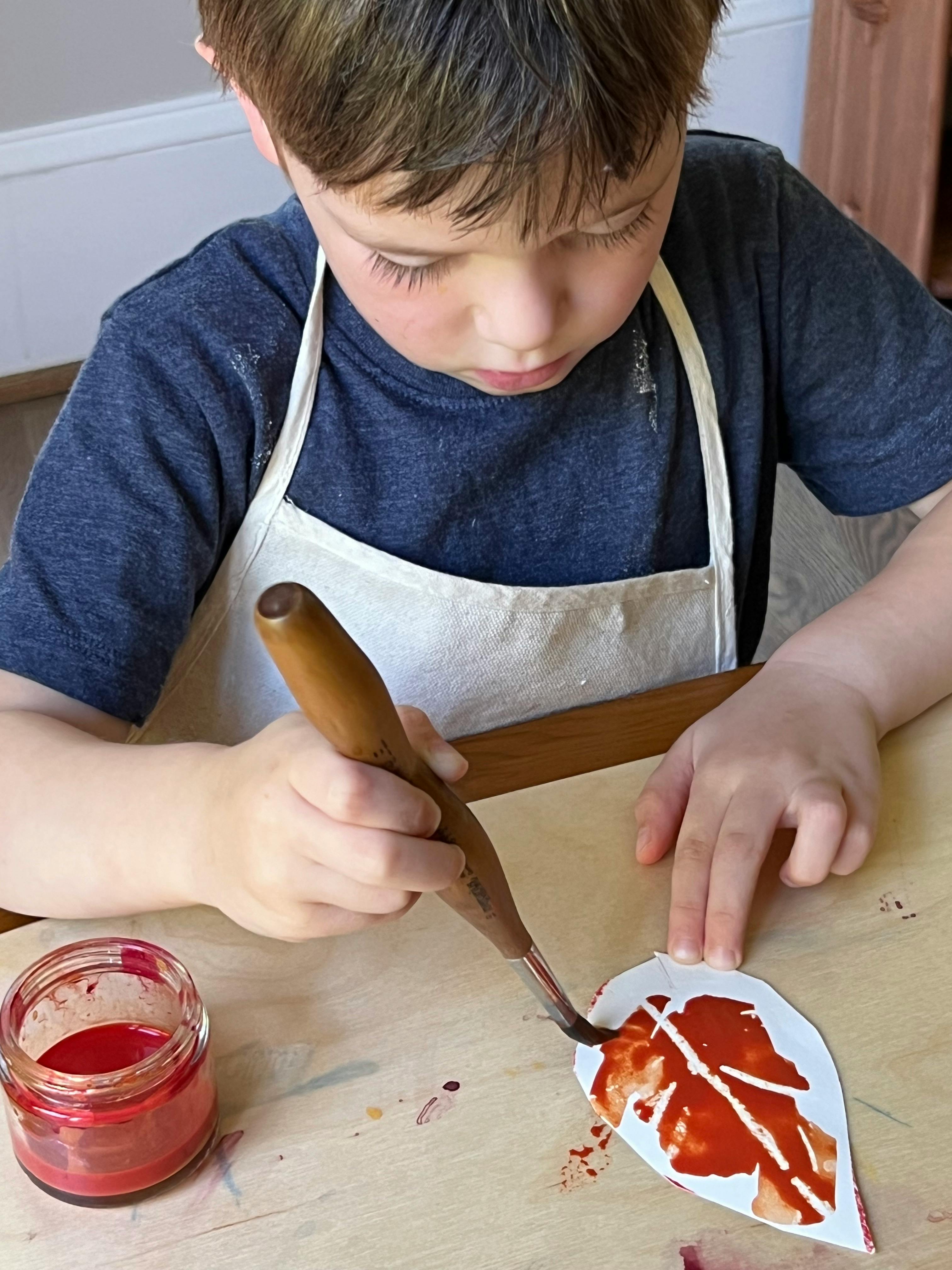 Child in an apron painting a leaf cutout with a brush