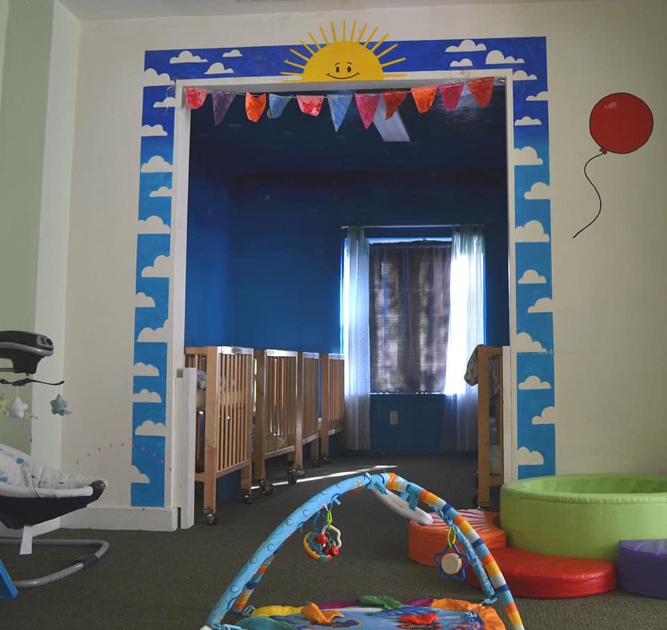 Doorway decorated with sun and clouds leading to a room with cribs