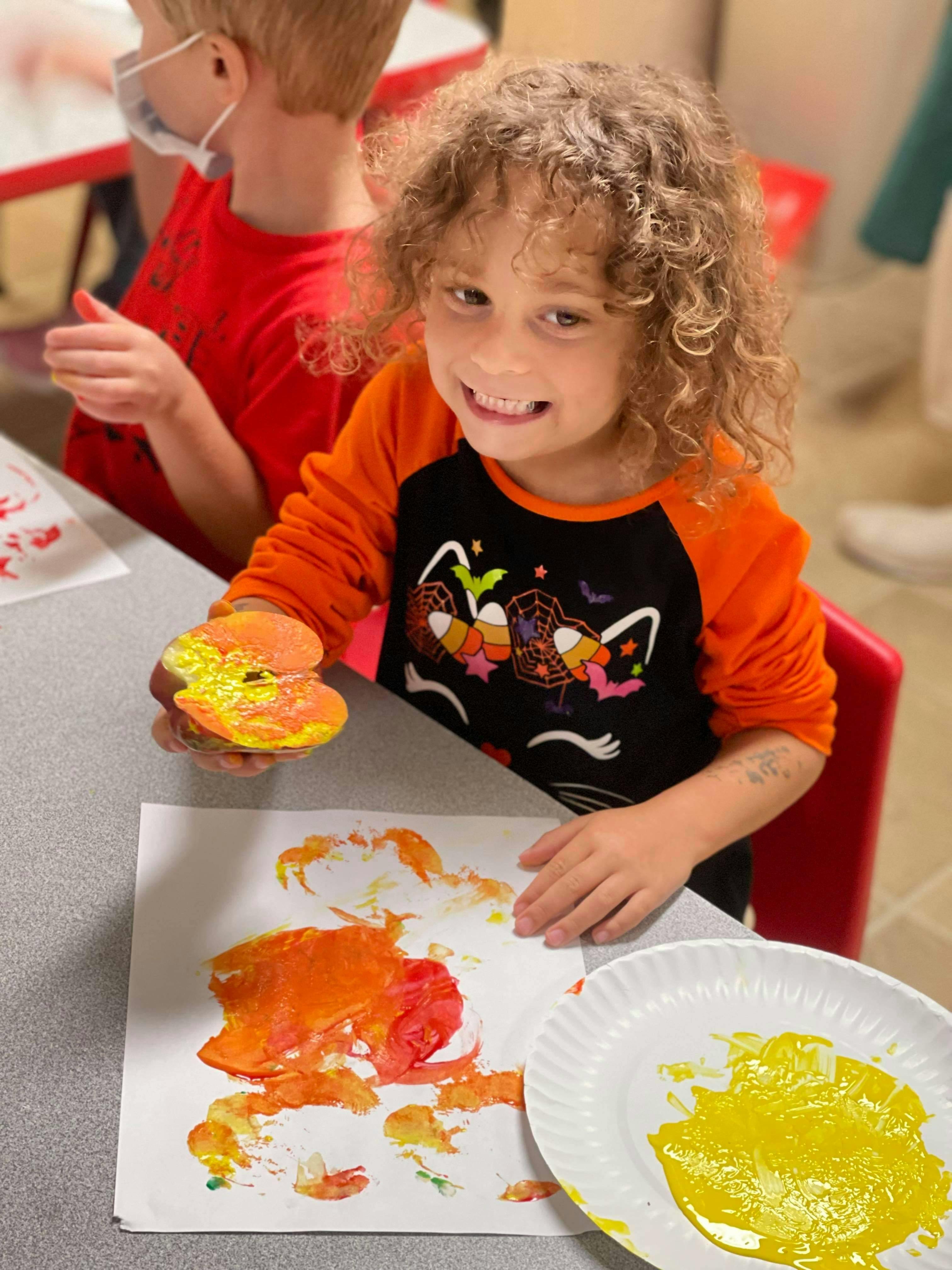 Child holding a painted apple stamp over a paper with paint