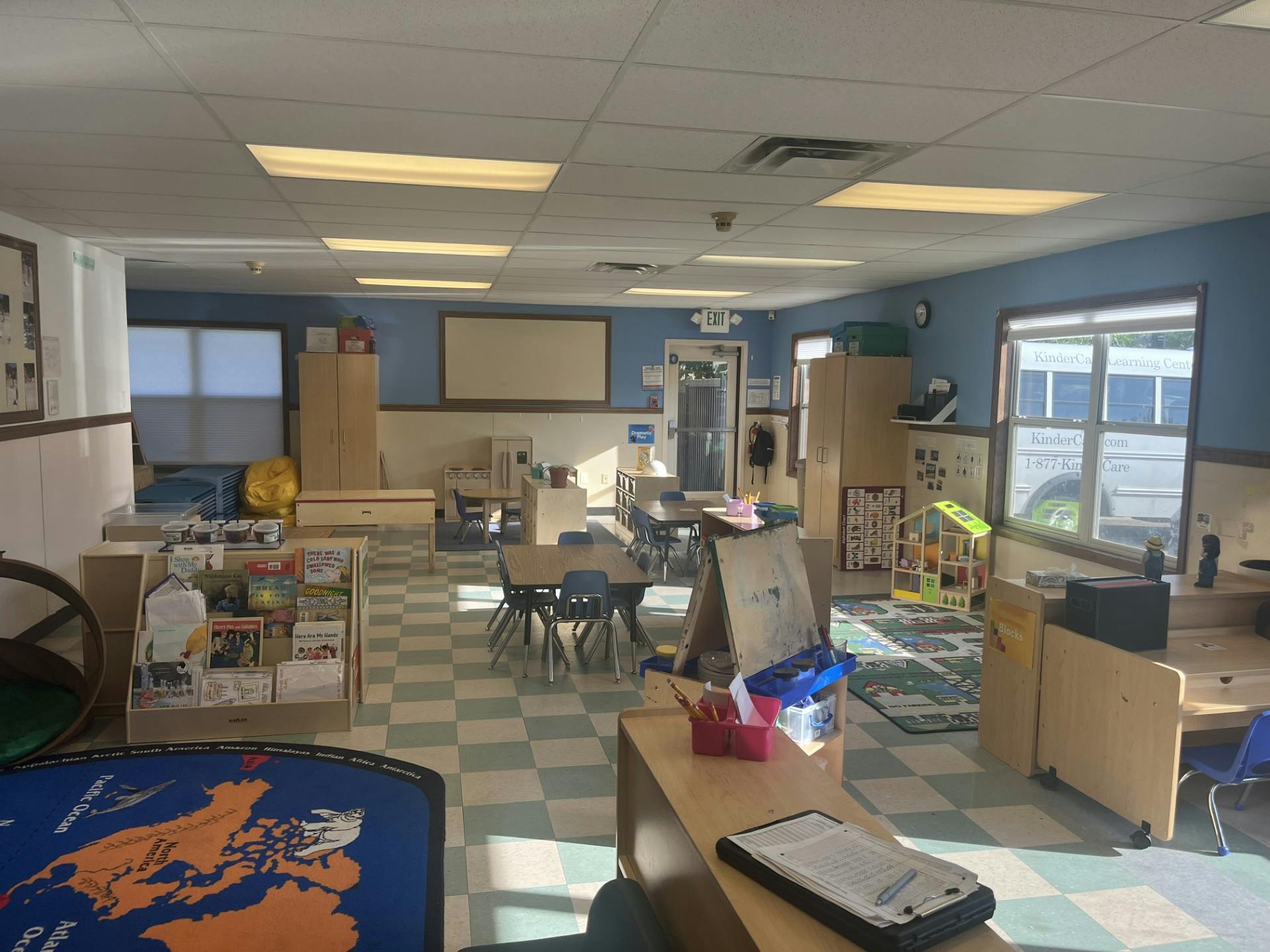 Classroom with small tables and chairs, a bookshelf, and a world map rug