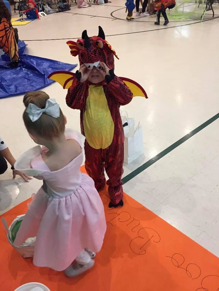 Child in dragon costume holding hands to eyes, child in pink dress