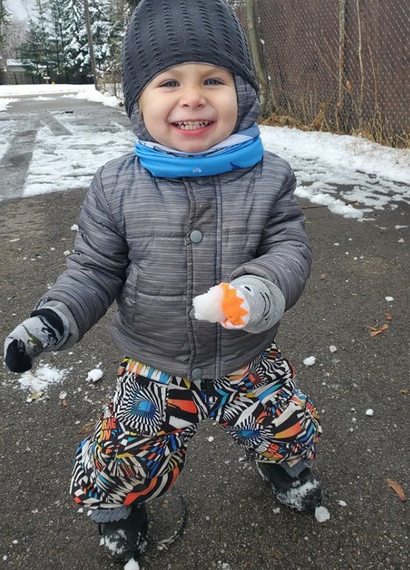 Child in winter clothing holding a snowball