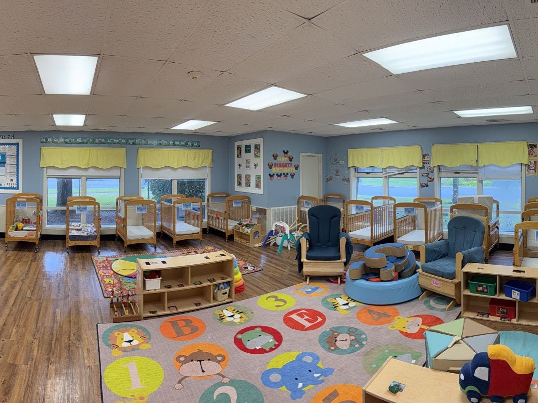 Baby room with multiple cribs, chairs, and colorful rug