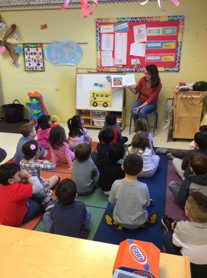 Adult reading a book to a group of children sitting on the floor in a classroom