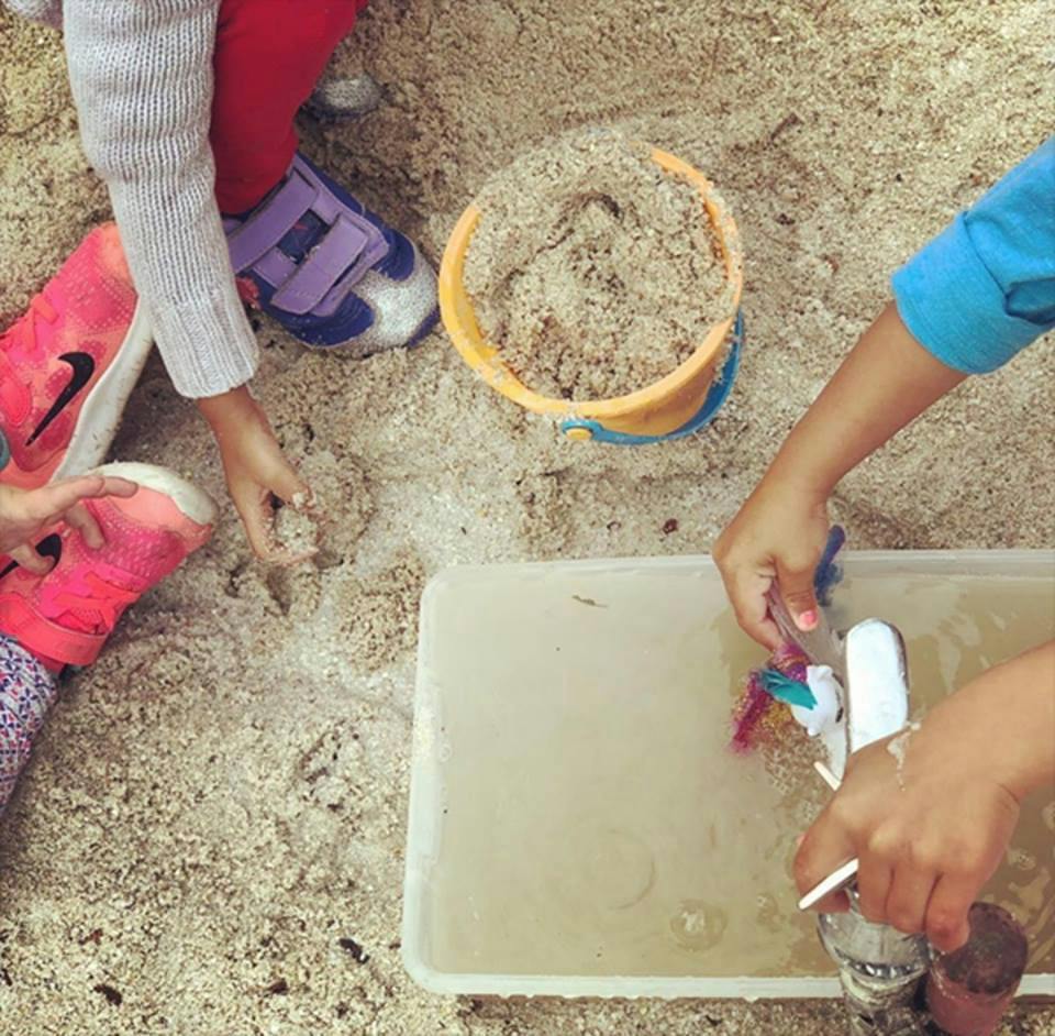 Children playing in sand with a bucket and water container