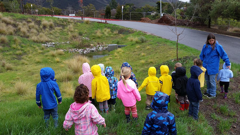 Adult and children in raincoats standing on a grassy hill