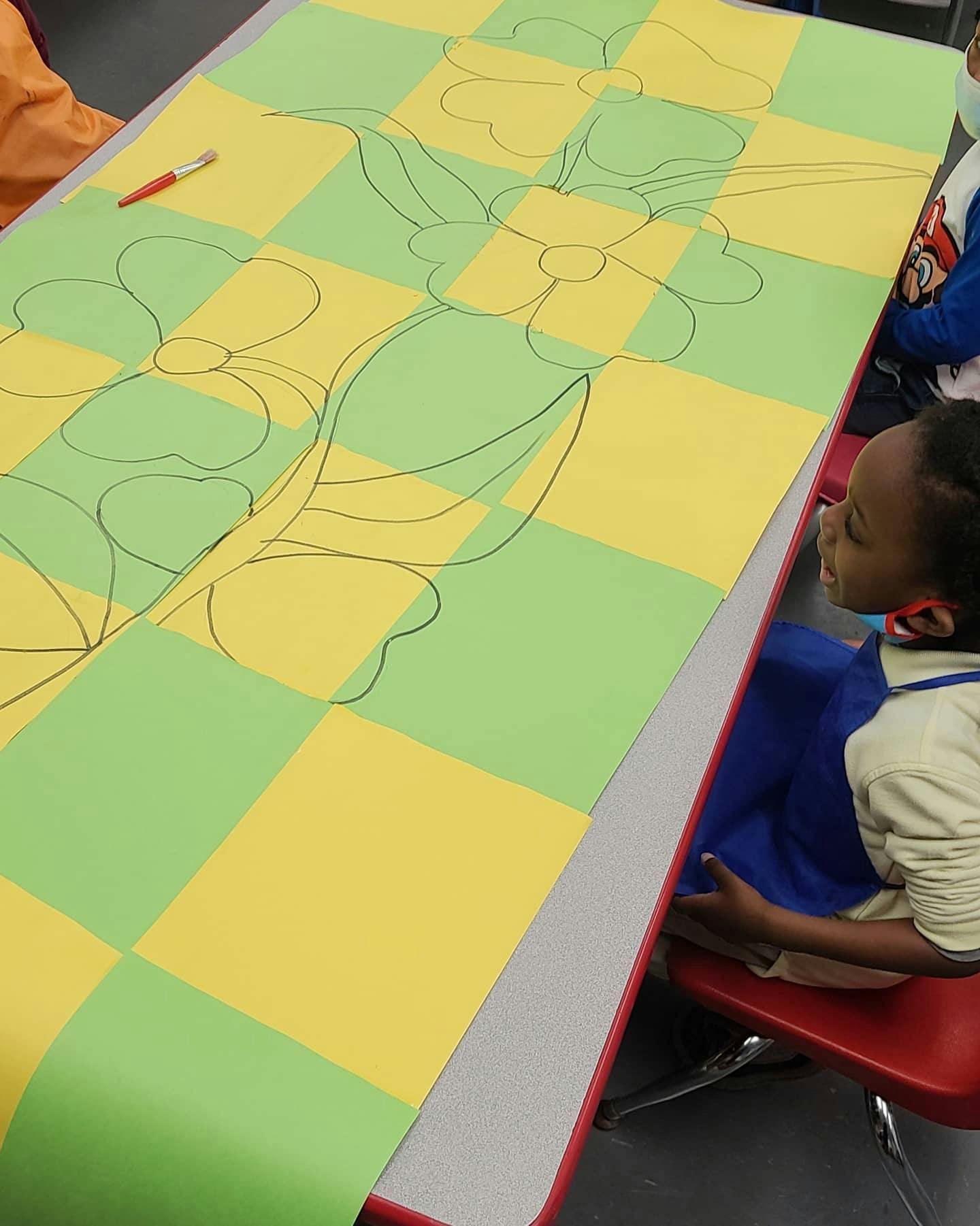 Child looking at a table with a checkered paper drawing of flowers