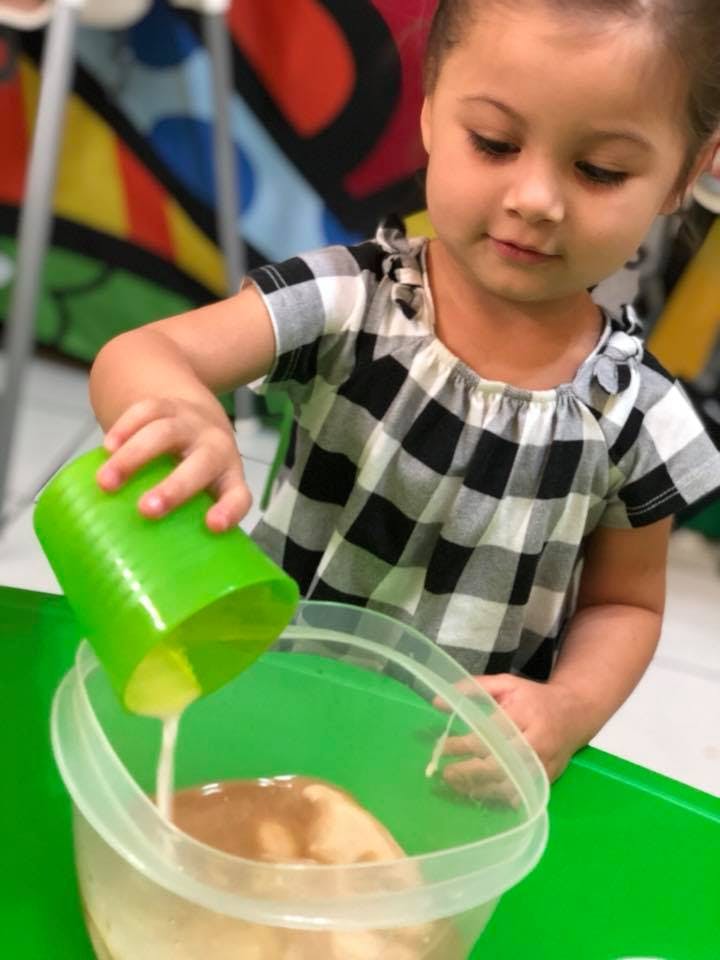 Child pouring liquid from a green cup into a clear container