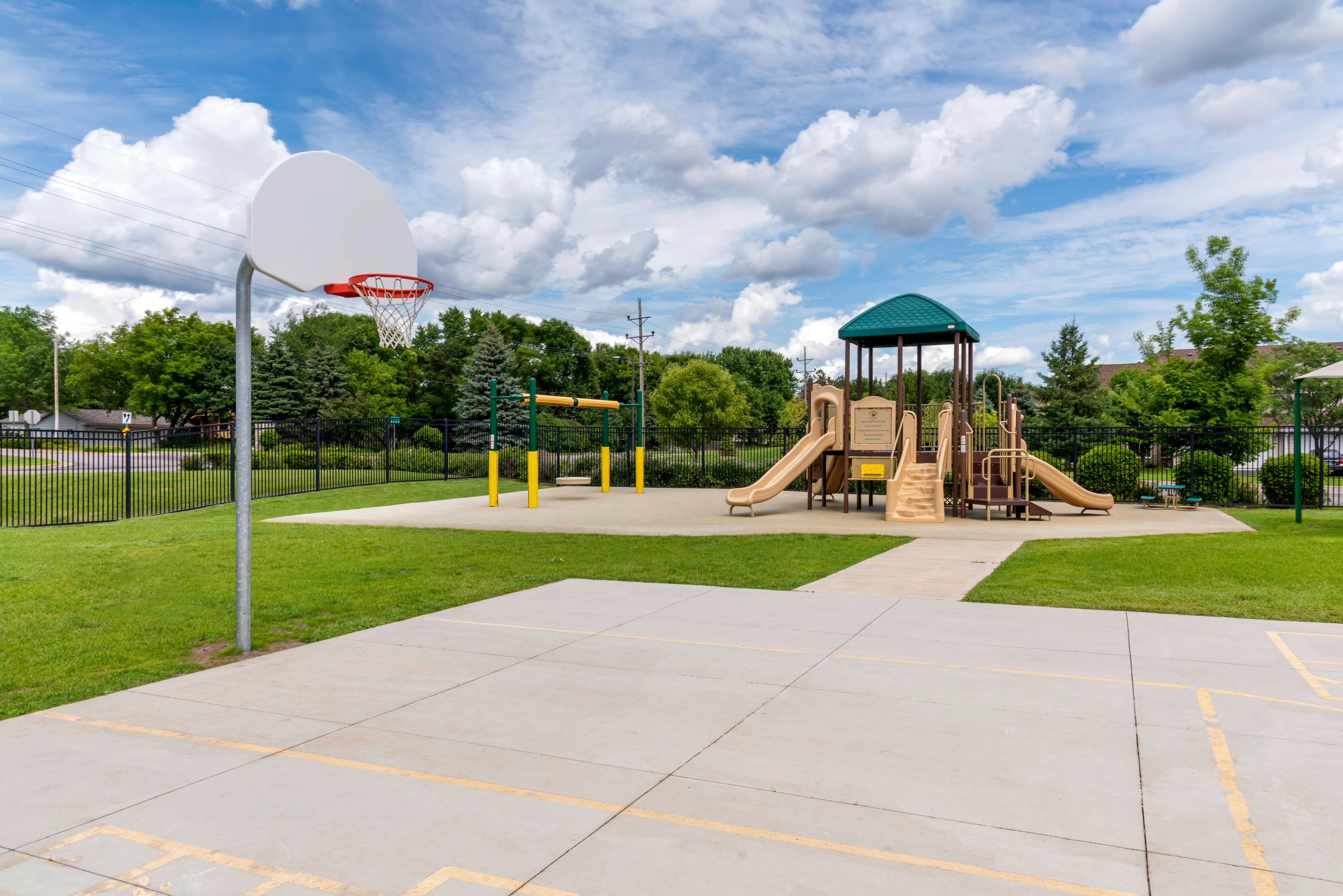 Basketball hoop on a court with a playground and swings behind it