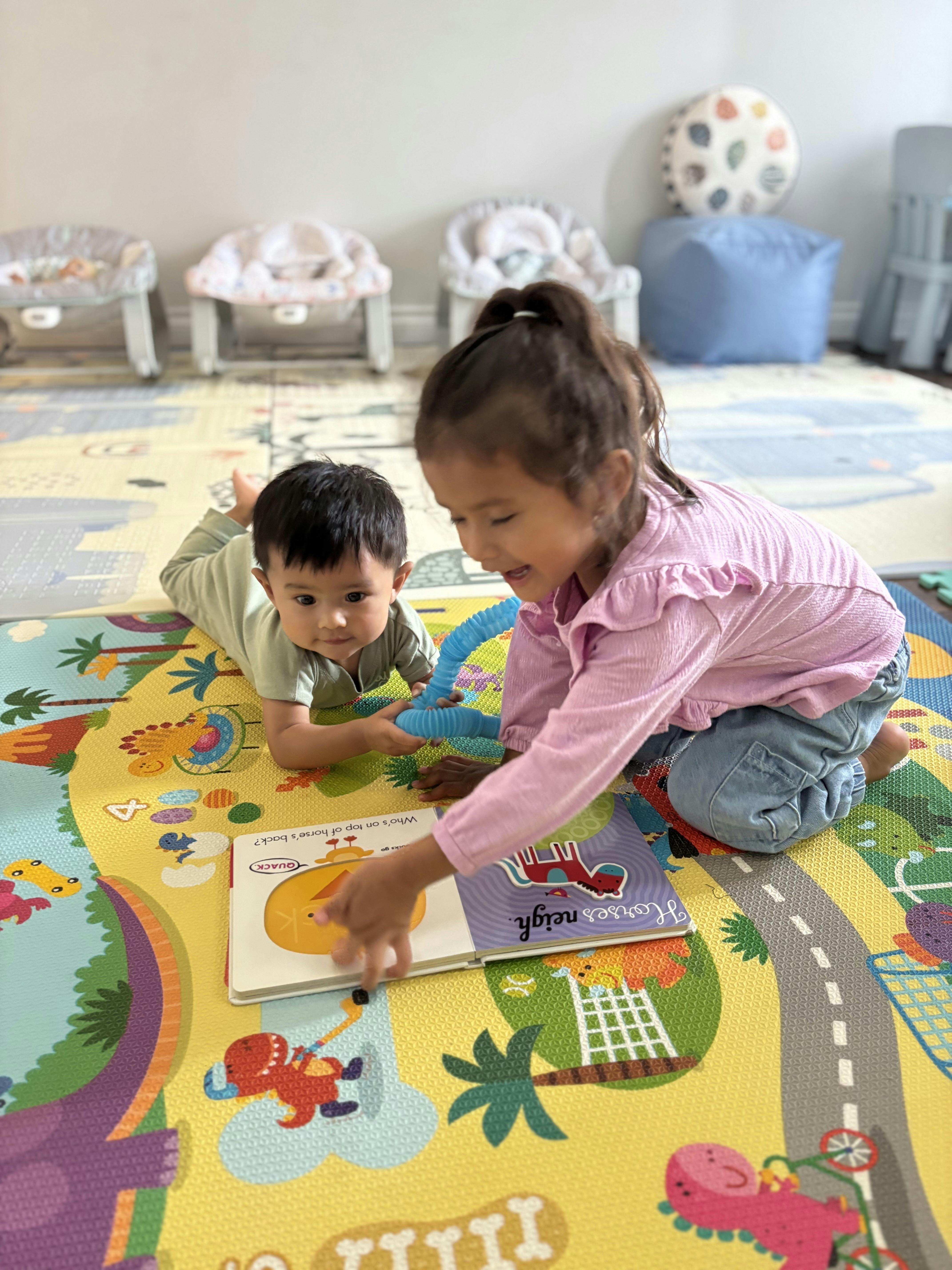 Two children playing with books and a toy on a colorful playmat