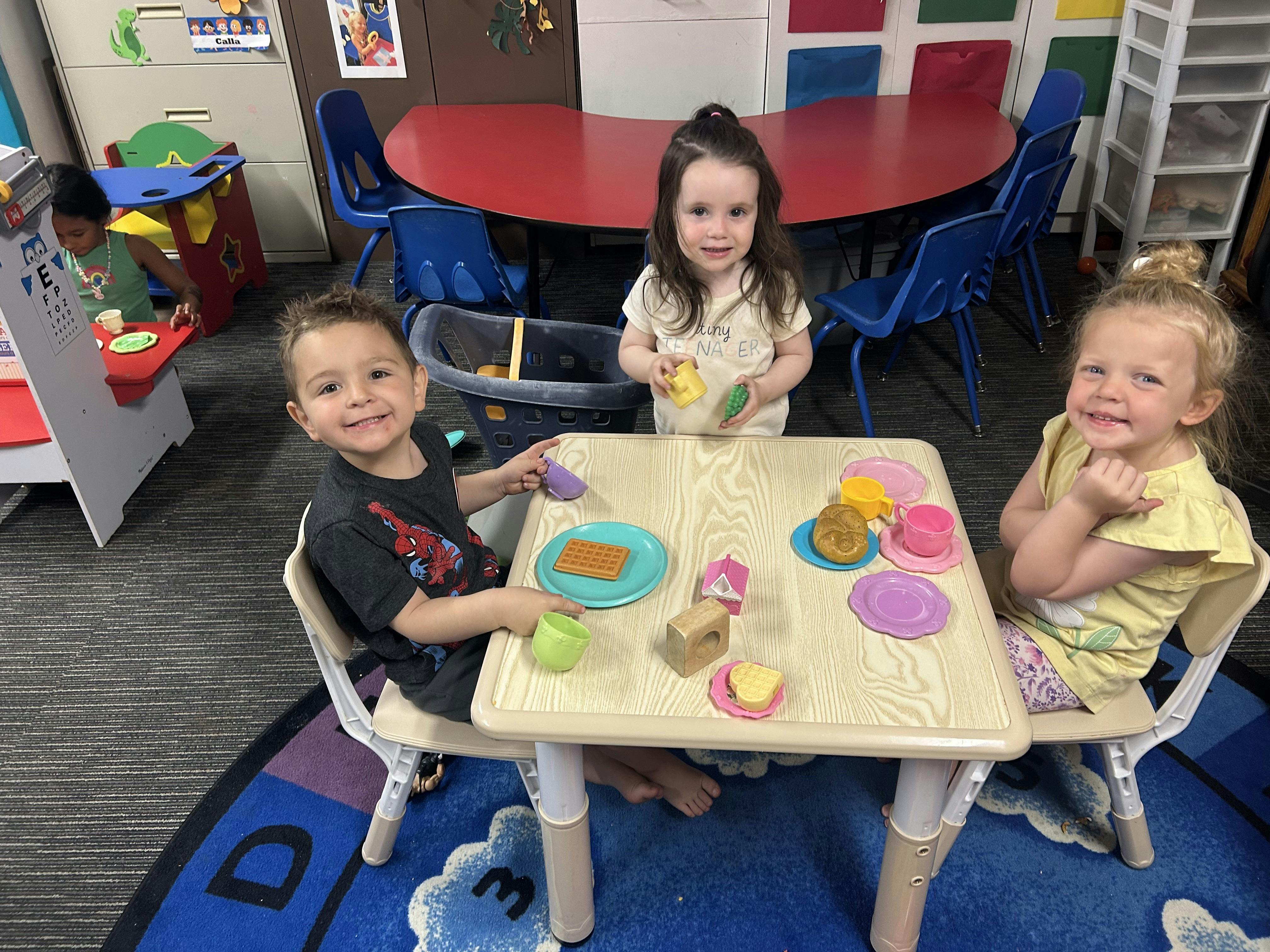 Three children playing with plastic toy food and dishes at a table