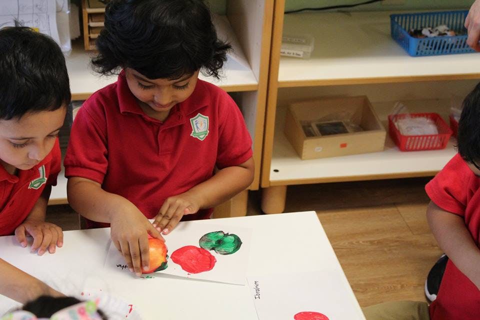 Child pressing an apple into paint on a table