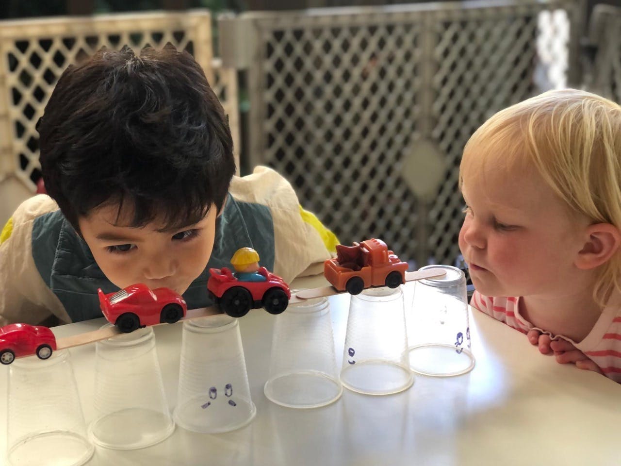 Two children looking at toy cars on top of plastic cups