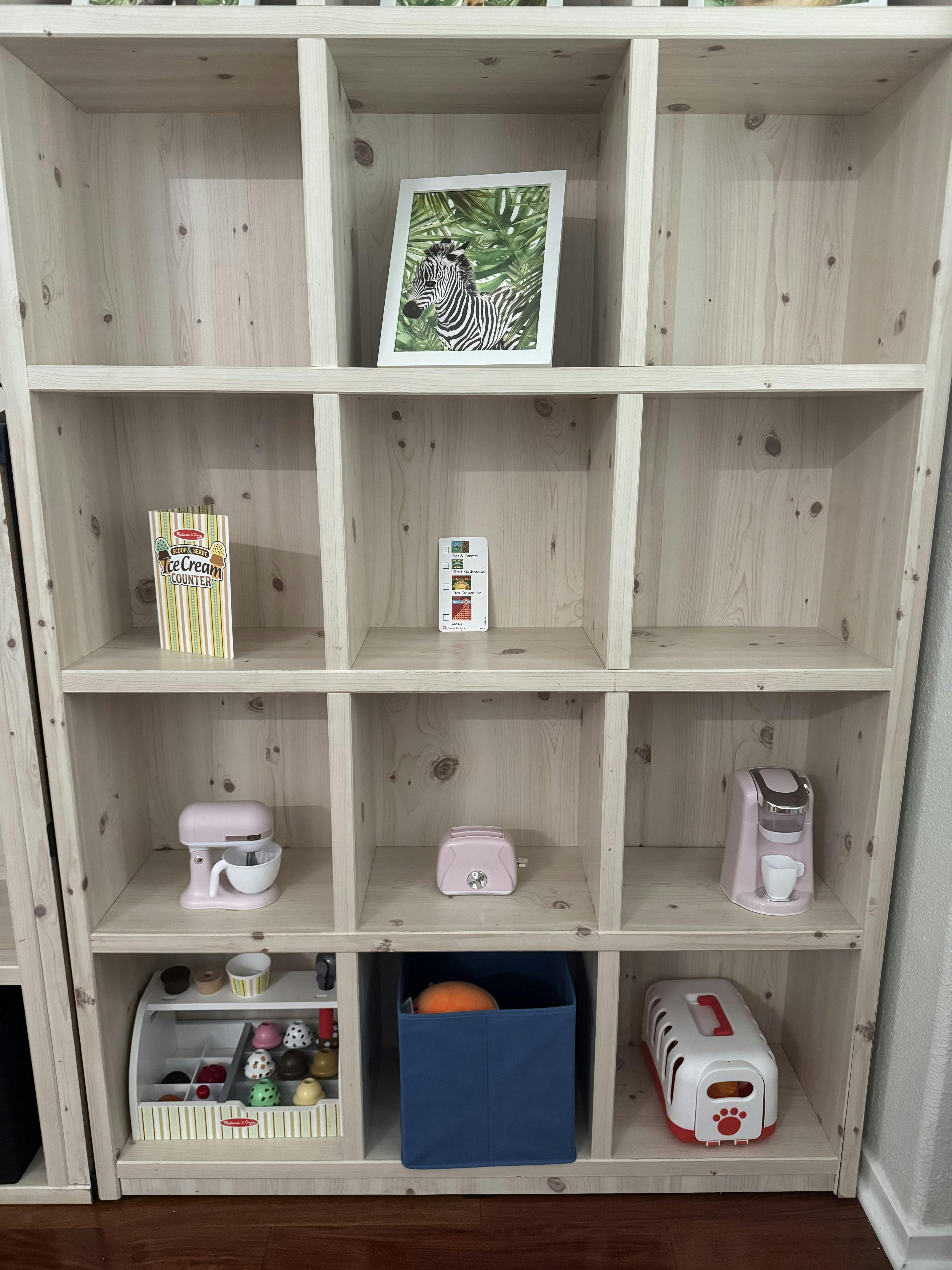 Wooden cube shelving unit with various toys and a framed zebra picture