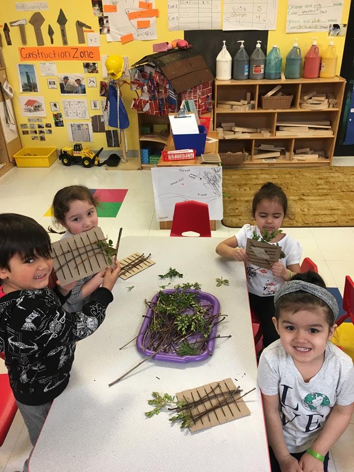 Four children at a table making crafts with leaves and sticks