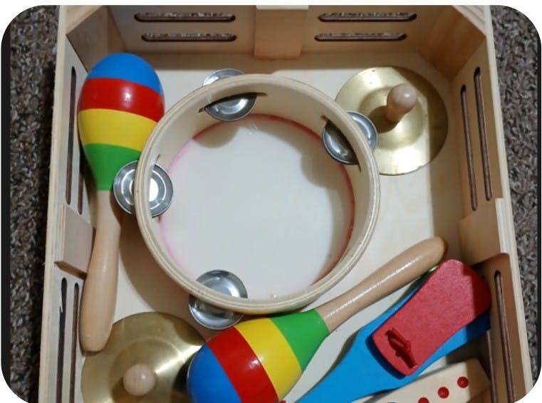 A tambourine, two maracas, and other musical instruments in a wooden box