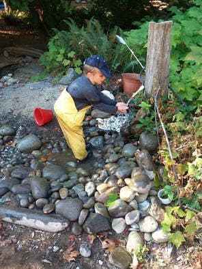 Child in yellow waders playing in a rocky stream