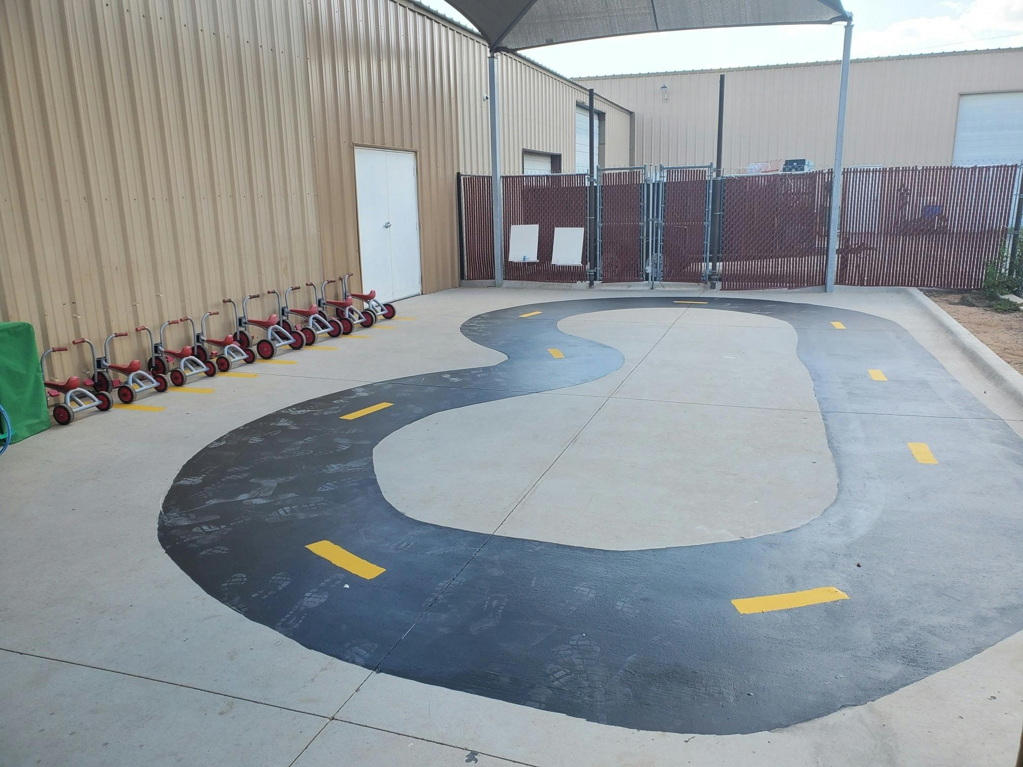 Outdoor play area with a painted track and tricycles lined up